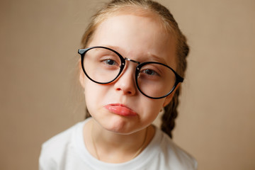 Sad little girl in glasses is looking with serious face at camera
