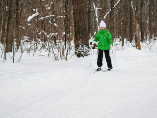 The girl moves on skis with sticks in the winter forest.