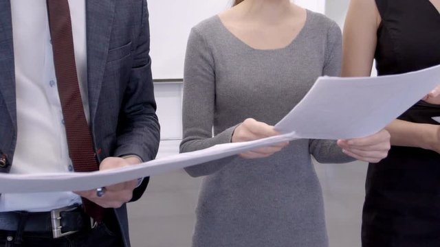 Three financial analytics are stanging in the conference room and holding the papers with bitcoin rates reports in their hands. Male and female traiders are preparing for the presentation about