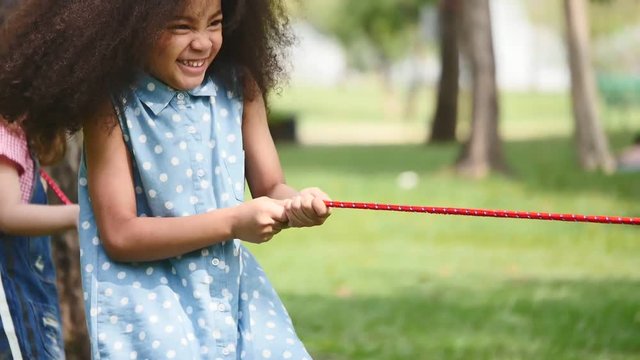 A little girl playing tug of war with her friends in a park