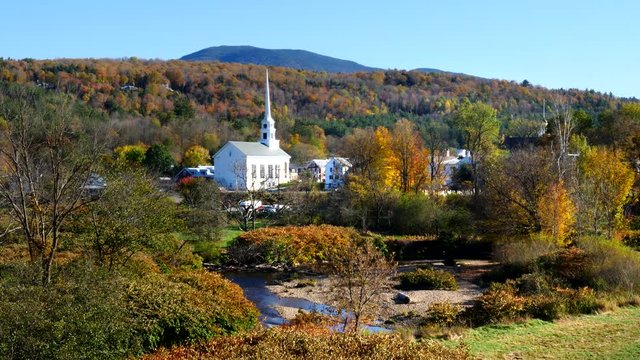 wide shot of a white new england church and a hillside covered in fall foliage at stowe in vermont, usa