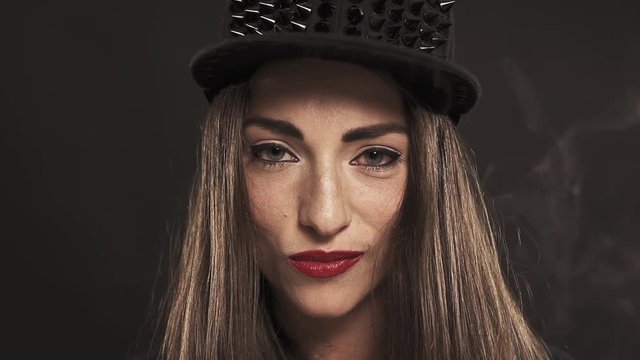 Young attractive caucasian brunette girl with red lipstick in spiked snapback cap smiling on black background