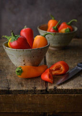 Sweet bell peppers in bowls on a wood surface with a knife