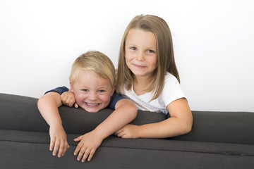 7 years old beautiful little girl posing happy at home sofa couch with her small cute young 3 years old brother in siblings love relationship