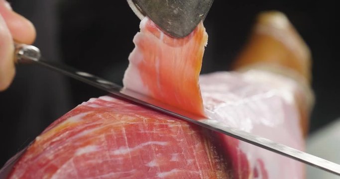 Close up macro of a chef who cuts a slice of ham, of excellent quality, with the knife according to tradition. Concept of: ham, food, Spain and Italy, catering.