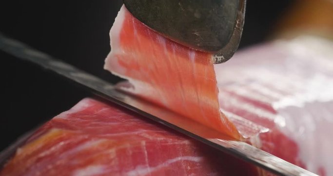 Close up macro of a chef who cuts a slice of ham, of excellent quality, with the knife according to tradition. Concept of: ham, food, Spain and Italy, catering.