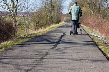 senior man with rollator on a bikeway and sunny winter day