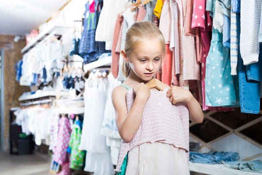 Little girl holding new dress in hands in boutique