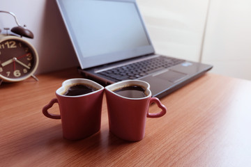Black coffee in  two cups heart shape and laptop computer on wooden floor