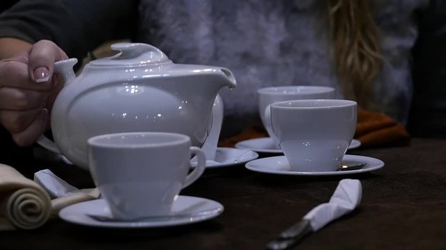 Woman pours herbal tea in a white mug in cafee. slow motion