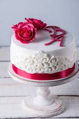 Beautiful white wedding cake decorated with flowers red roses and ribbon. Concept of elegant holiday desserts