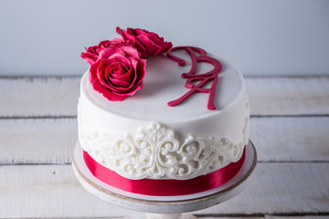 Obraz na płótnie Canvas Beautiful white wedding cake decorated with flowers red roses and ribbon. Concept of elegant holiday desserts