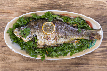 Fried fish carp in plate on wooden background, top view