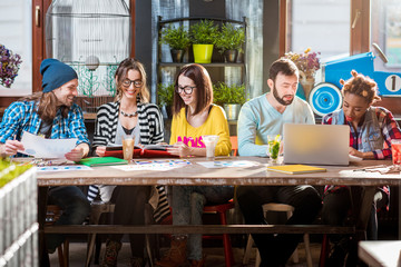 Group of friends dressed casually working or studying together at the big table in the modern cafe intreior