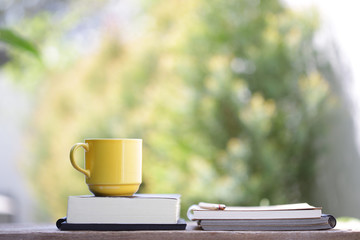 Yellow cup with books on wooden table at outdoor