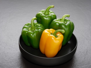 Yellow and green bell pepper or capsicum in shallow black bowl over dark background