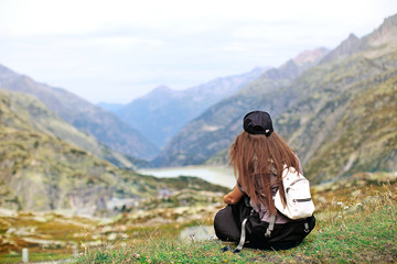 girl with a backpack sits with her back near the cliff, mountain view