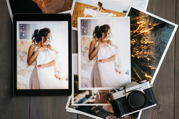 Printed wedding photos with the bride, a vintage black camera and a black tablet with a picture of...