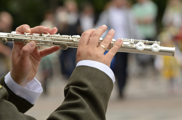 A musician’s hands playing the silver flute in front of blurred motley background
