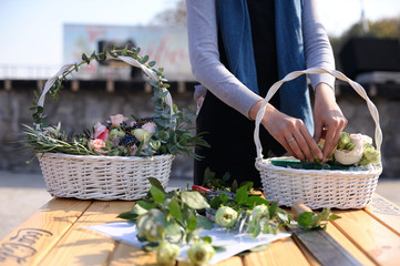Floristry teaching outdoor. A woman setting bunch of flowers on a wooden desk, a basket with...