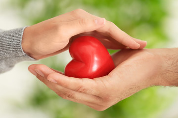 Man and woman holding small red heart in their hands on blurred background