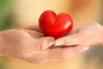 Man and woman holding small red heart in their hands on blurred background
