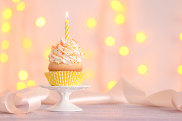 Birthday cupcake with candle on stand against blurred lights
