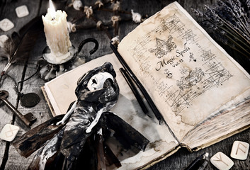 Old book with evil spells, scary doll, rune and burning candle on planks. Halloween, occult,...