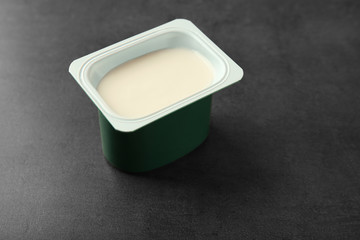 Plastic cup with yogurt on dark background