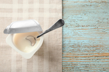 Plastic cup with yogurt on wooden background