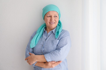 Mature woman with cancer in headscarf on light background