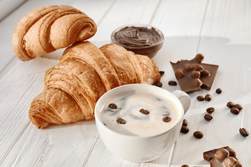 Tasty croissants with cup of coffee and chocolate sauce on wooden table
