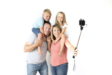 lovely young couple taking selfie photo self portrait with stick and mobile phone carrying son and daughter on shoulders posing happy smiling