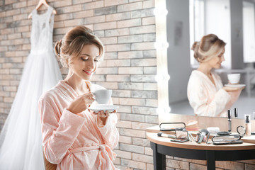 Beautiful young bride drinking coffee in makeup room