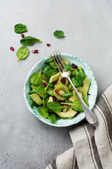 Salad of spinach baby leaves, watercress, kiwi, avocado and pomegranate in old ceramic plate on gray concrete background. Selective focus. Top view. Copy space.