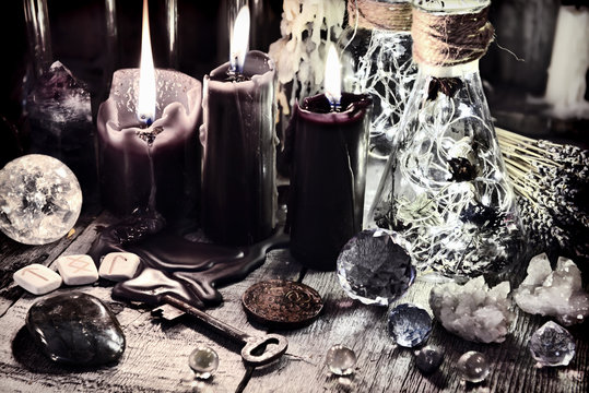 Black candles, crystals and stones, ancient runes, key and ritual bottles on witch table Halloween, occult, esoteric and wicca concept. Vintage background