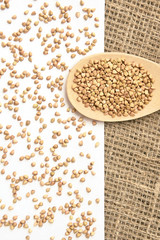 Scattered buckwheat grains. White background. Wooden spoon