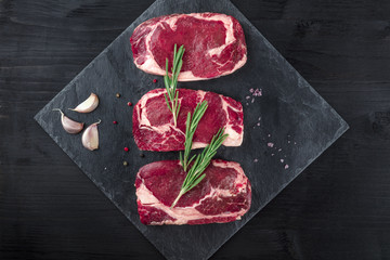 Three slices of raw meat on black with seasoning