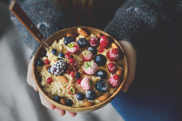 Woman hands holding oatmeal porridge with frozen berries, almonds in wooden bowl. Banner. Healthy breakfast. Clean eating, detox diet. Vegetarian, raw, vegan concept