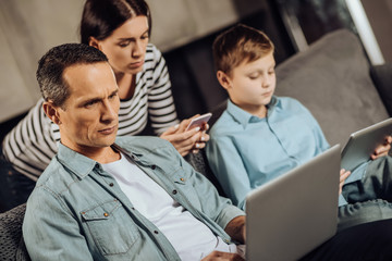 Addicted to gadgets. Pleasant young family sitting on the couch and having their attention solely...