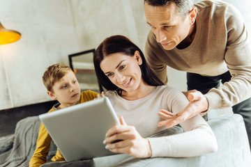 Not caring. Pleasant young man scolding his wife for being glued to her tablet while her little son...