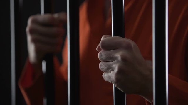 Hands of angry arrested male gripping prison bars, unfair judgment, closeup