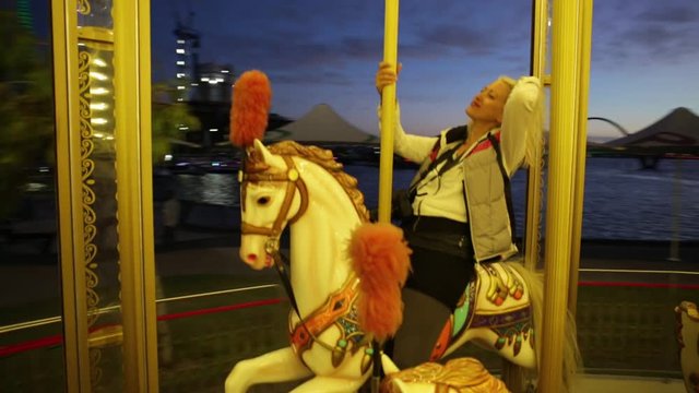 Carefree blonde caucasian woman amuses on white horse of Perth city, Western Australia. Perth skyline on background by night. Leisure and recreational concept.