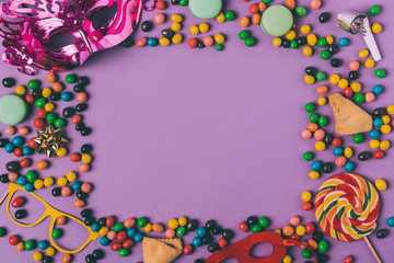 top view of arranged masquerade masks, candies and cookies isolated on purple