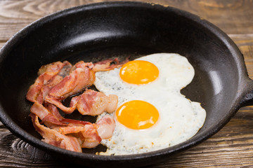 Bacon and Egg. Salted egg and sprinkled with black pepper. English breakfast. Grilled bacon, two eggs on pan on wooden table.