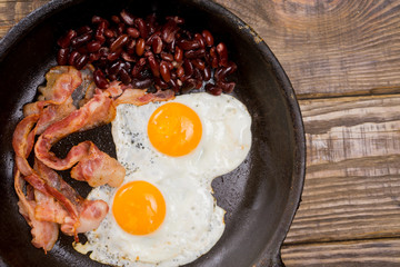 Bacon,Egg and bean. Salted egg and sprinkled with black pepper. English breakfast. Grilled bacon, two eggs and beans in pan on wooden table