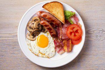 Full English or Irish breakfast: sausages, bacon, egg, mushrooms, tomatoes and toasts. Nutritious morning meal