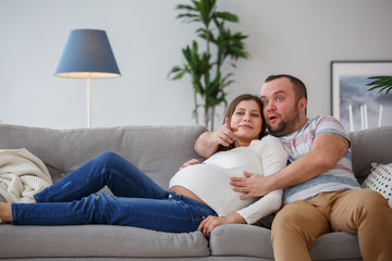 Fototapeta na wymiar Image of happy pregnant woman and man sitting on gray sofa