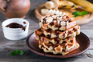 Belgian waffles with chocolate syrup and banana slice on a plate on a wooden background
