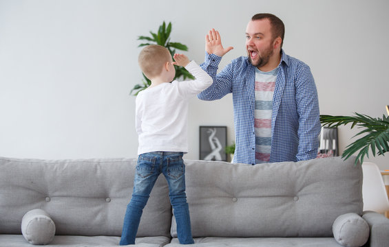 Family picture of young son standing on couch doing handshake with father